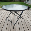 Round glass table on a wooden deck with potted plants in the background